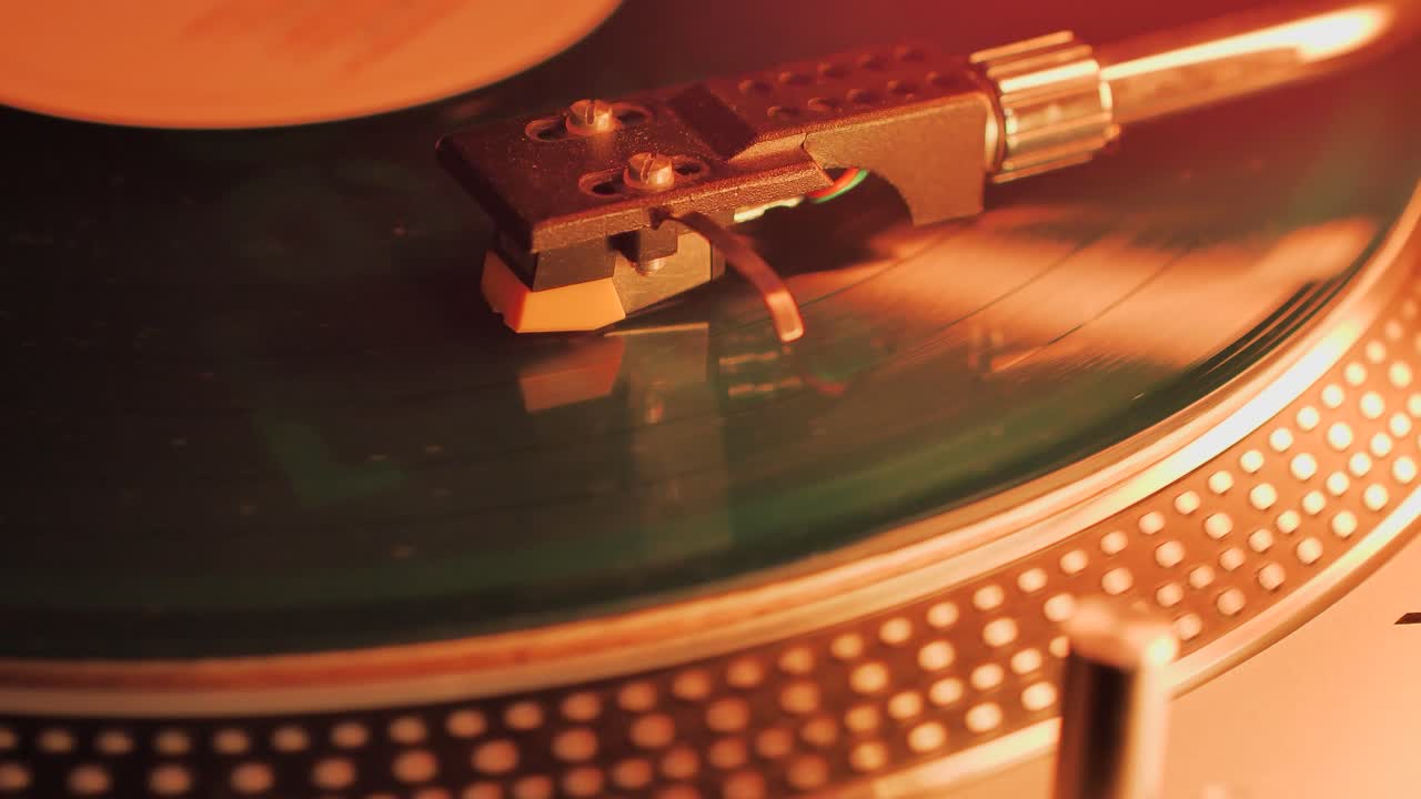 A Rotating Vinyl Record on a Turntable in the Light of a Warm Orange-Red Lamp. A dusty green colour LP Vinyl Disc Record Close-up Playing Music. Type D.
