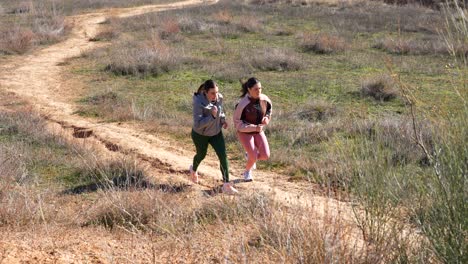 dos mujeres corriendo cuesta arriba en terreno accidentado durante una sesión de entrenamiento