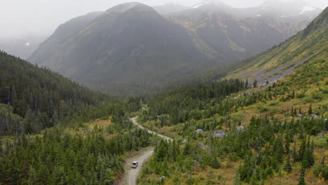 wide aerial of truck driving dirt road through british columbia mountains