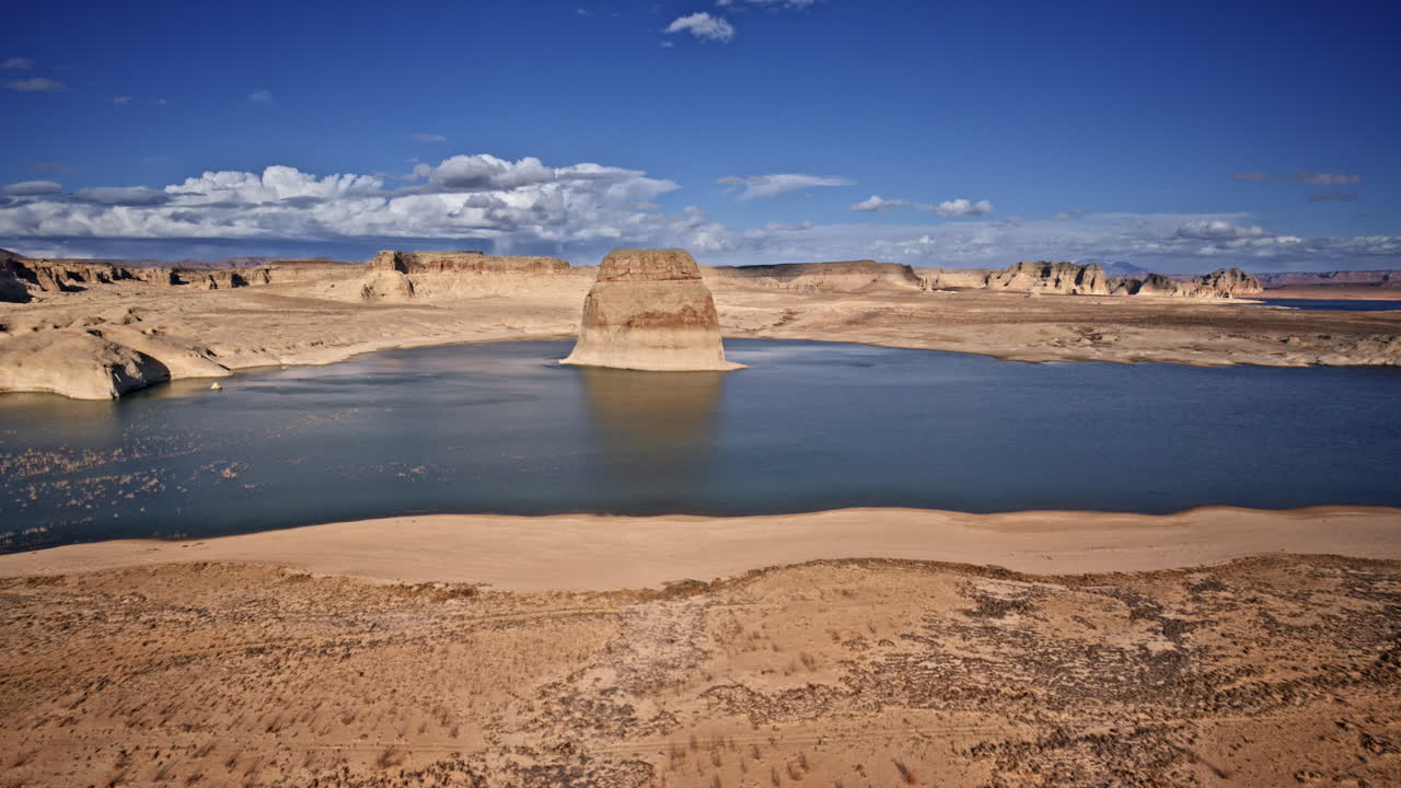 Sweeping aerial view of an isolated rock monolith in Lake Powell, set against a dramatic canyon landscape near Page, Arizona.