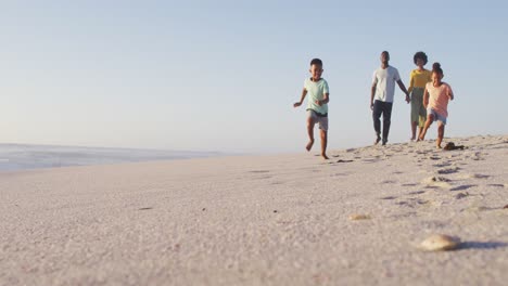 Familia-Afroamericana-Sonriente-Caminando-Y-Tomados-De-La-Mano-En-La-Playa-Soleada