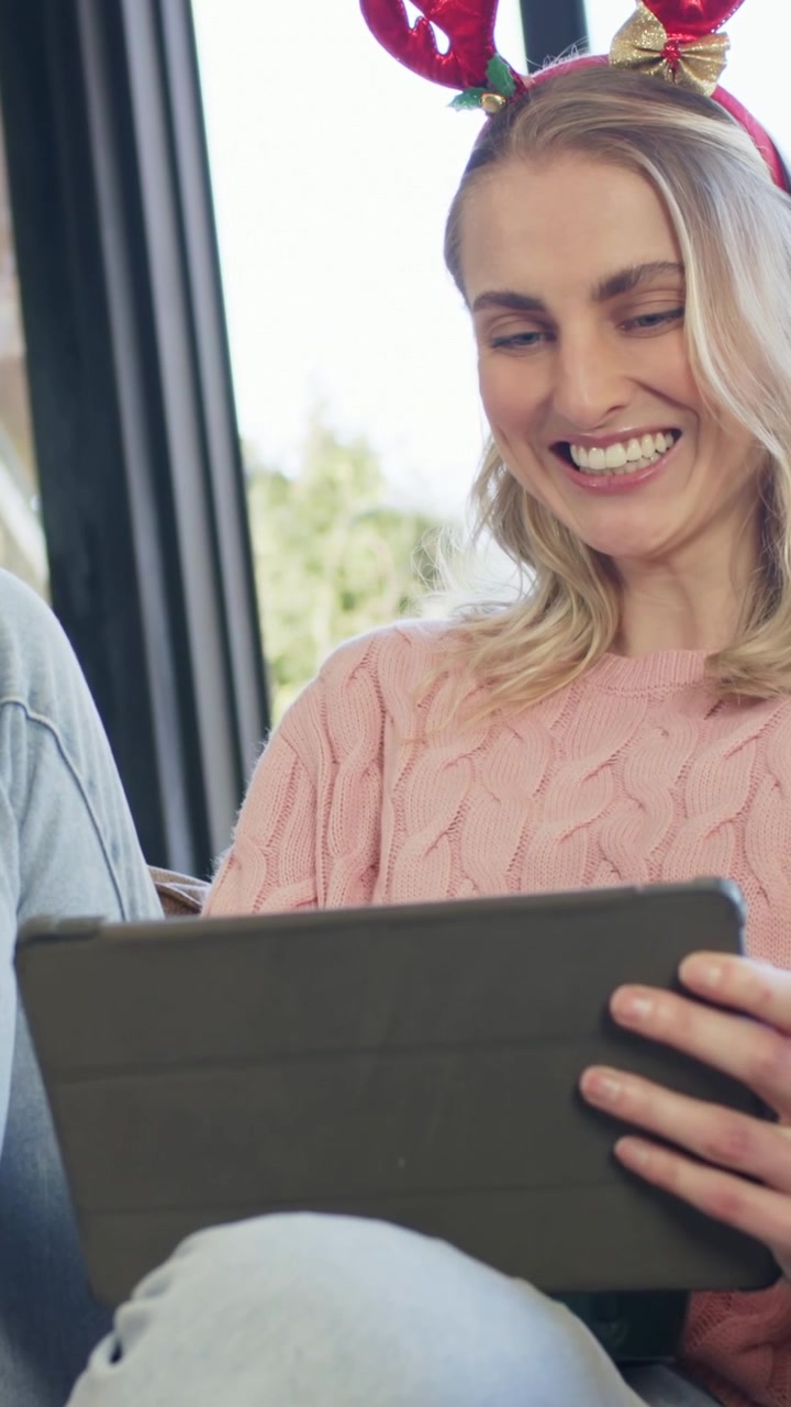Vertical video: Seeing tablet clip woman pink sweater antlers putting green mug aside at home