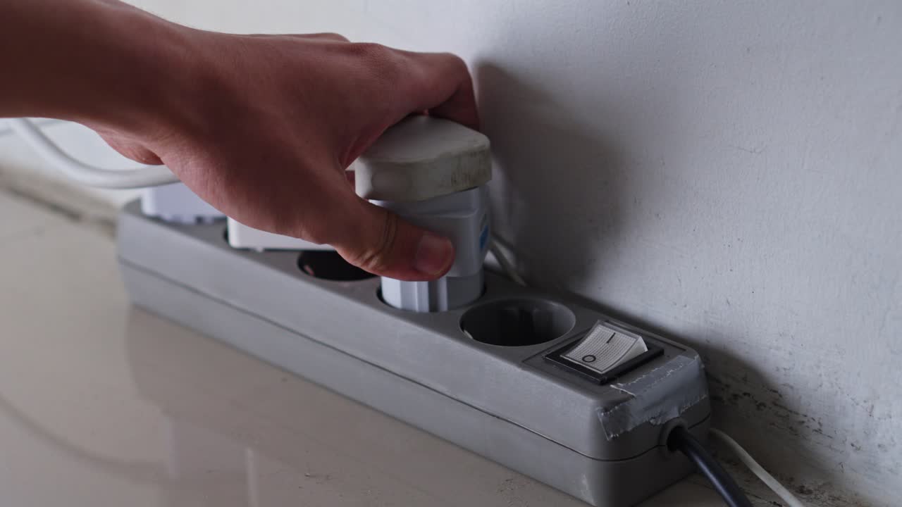 Close-up of hand disconnecting multiple plugs from power strip to reduce standby consumption