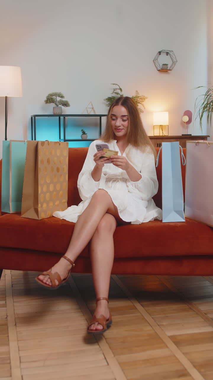 소파 에 앉아 있는 신용 카드 로 온라인 지불 을 하는 쇼핑 가방 을 가진 행복 한 쇼핑 중독자 여자