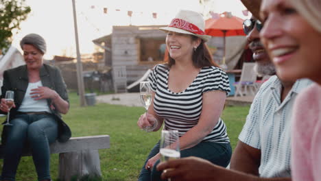 group of mature friends sitting around fire and drinking at outdoor campsite bar