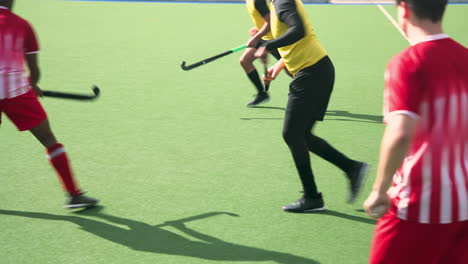playing field hockey, men running and holding sticks on outdoor field