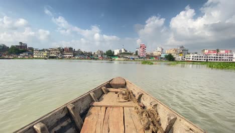 pov view of rowing wooden boat at buriganga river. dhaka city in front with sunny blue sky with clouds