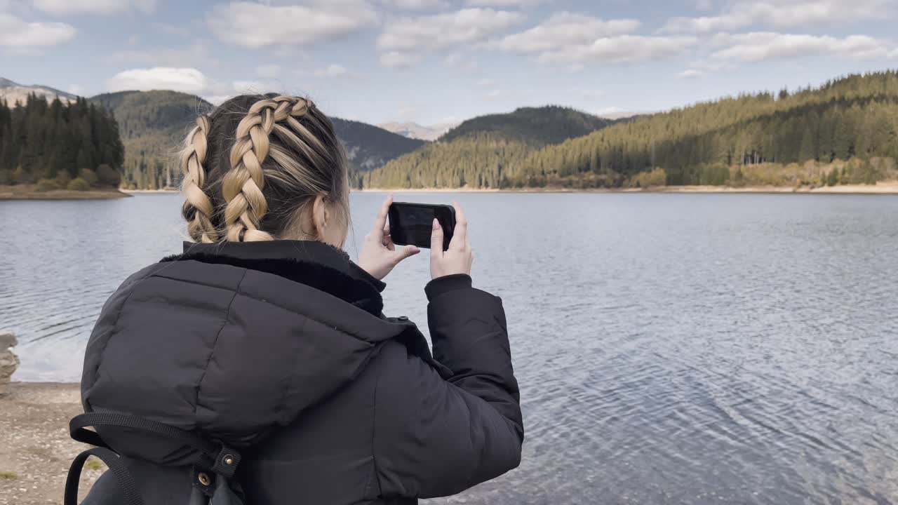 mujer con un teléfono móvil tomando una foto del lago bolboci en rumania