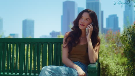 relaxed girl talking by iphone in park. asian lady speaking phone outdoors.