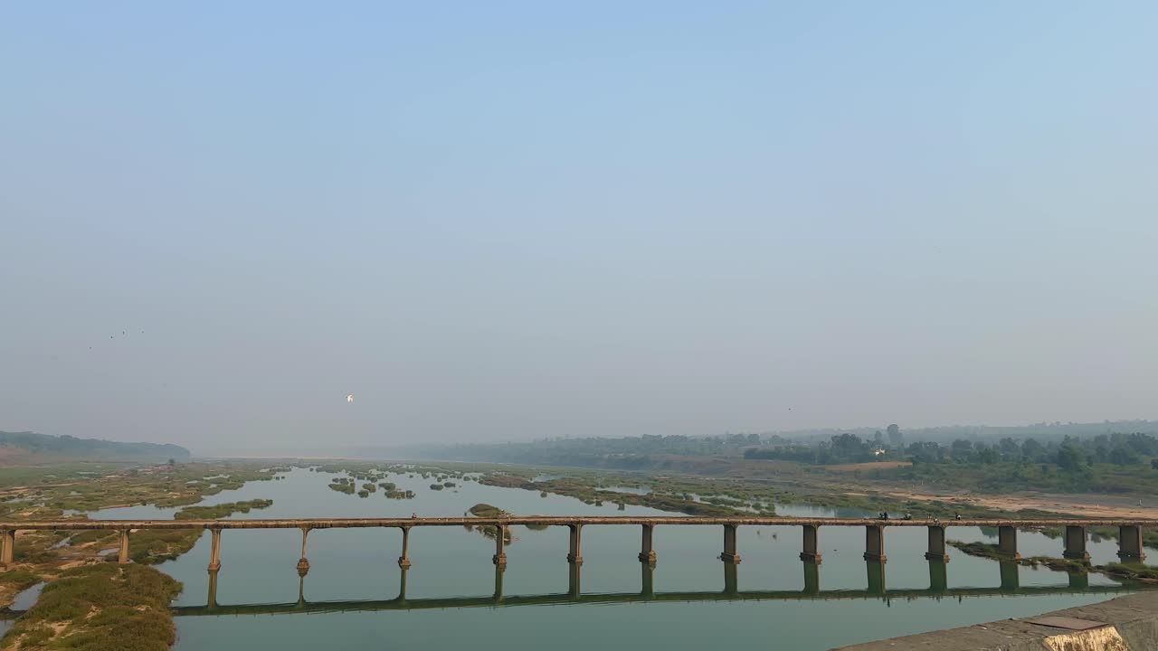 Jembatan beton tua membentang di atas Sungai Son yang tenang, pilar-pilarnya terpantul di perairan dangkal dan hamparan pasir, dikelilingi oleh langit terbuka dan perbukitan hijau yang jauh