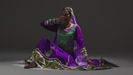 Female-Kathak-Dancer-Performing-Dance-Wearing-Traditional-Indian-Dress-Seated-On-Floor-In-Spotlight-4