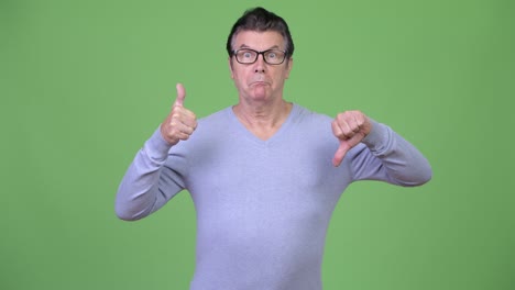 Senior handsome man choosing between thumbs up and thumbs down