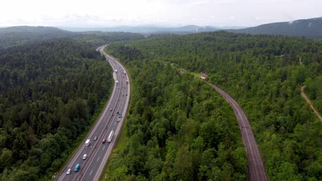 Europäische-Autobahn-Und-Eisenbahn-Direkt-Nebeneinander,-Umgeben-Von-Einem-Grünen-Gürtel-Aus-Hohen-Bäumen