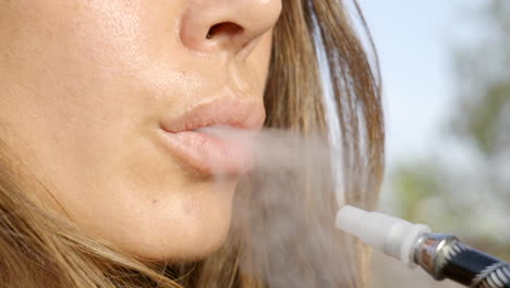 closeup of woman's lips exhaling smoke from electronic cigarette