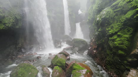 drone pullback from mist at bottom of secluded falls in ravine of jungle