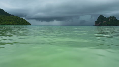 dolly aérea volando bajo por encima del agua verde brillante a las nubes negras grises tormentosas por encima del océano, koh phi phi tailandia