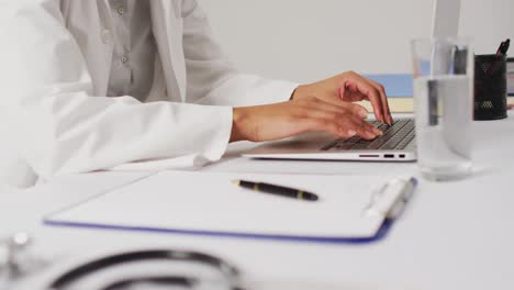 Video-of-biracial-female-doctor-using-laptop-on-blue-background