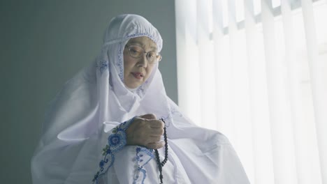 una mujer mayor sostiene cuentas para el dhikr después de hacer el salat