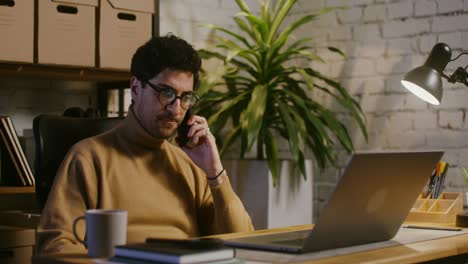 hombre trabajando desde casa por la noche, emocionado por una llamada telefónica