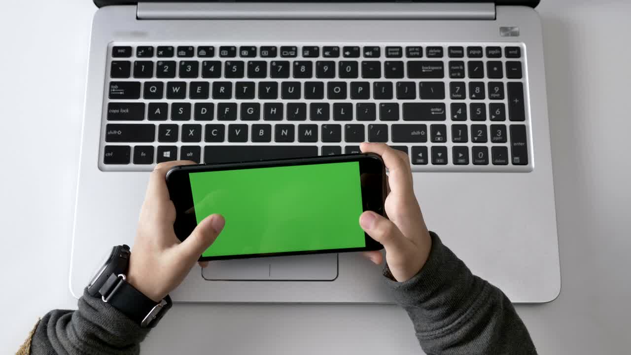 Children's hands playing on a smartphone, Green screen, chromakey concept, laptop in the background. Top shot 60 fps