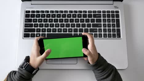 children's hands playing on a smartphone, green screen, chromakey concept, laptop in the background. top shot 60 fps