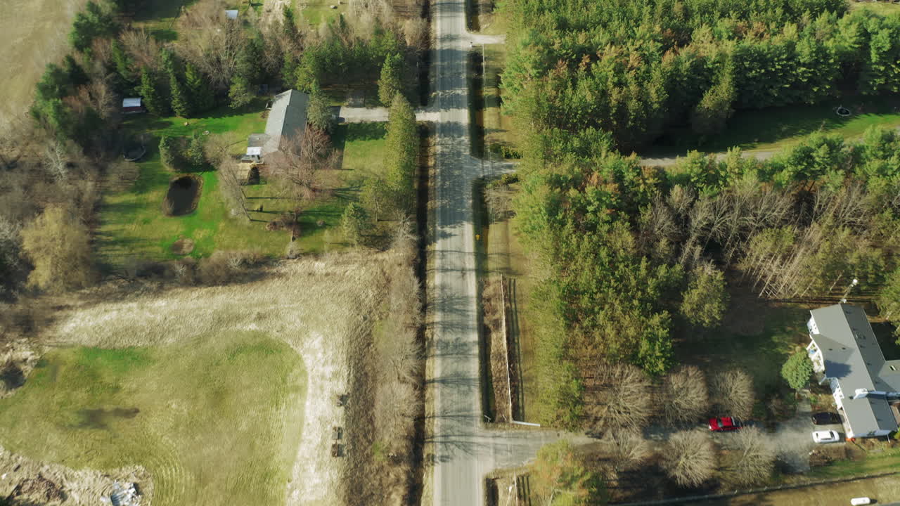 pequeño camino de dos carriles en una calle rural con propiedades y casas a cada lado