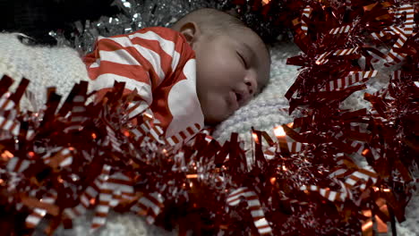 adorable cute 2 month old indian baby boy in festive outfit sleeping surrounded by red and silver tinsel