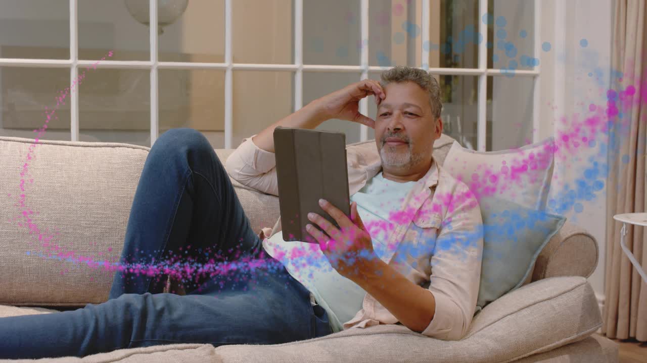 Mature man lounging on sofa tapping tablet, causing pink or blue swirls encircling him for tech demo