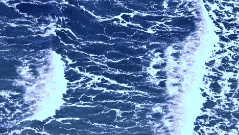 drone captures turbulent ocean waves breaking over deep blue water near port douglas, australia. bright daylight, top-down perspective, steady camera movement