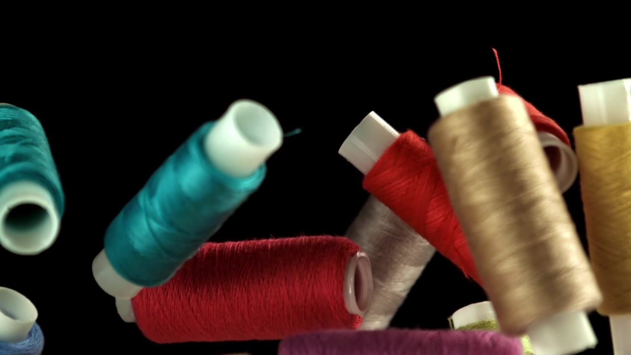 Multi-colored Sewing Thread Spools Falling Against Black Background