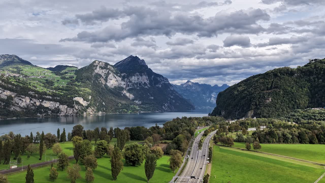 Timelapse aerial view of Walensee in Switzerland, showing mountains reflected in the calm lake, a winding road, and moving clouds in the sky