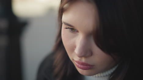 close-up of young girl with pink lips and nose ring, eyes downcast, thoughtful expression, hair softly falls, with blurred background of warm colors