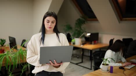 Focused-brunette-woman-walking-with-laptop-by-office-with-coworkers,-trying-to-solve-the-problem