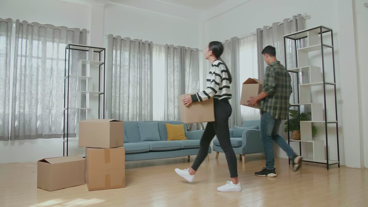 행복한 젊은 아시아 커플이 새로운 집으로 물건을 담은 카드보드 상자를 운반하는 것을 축하합니다. 그들은 함께 새로운 집으로 이사합니다.