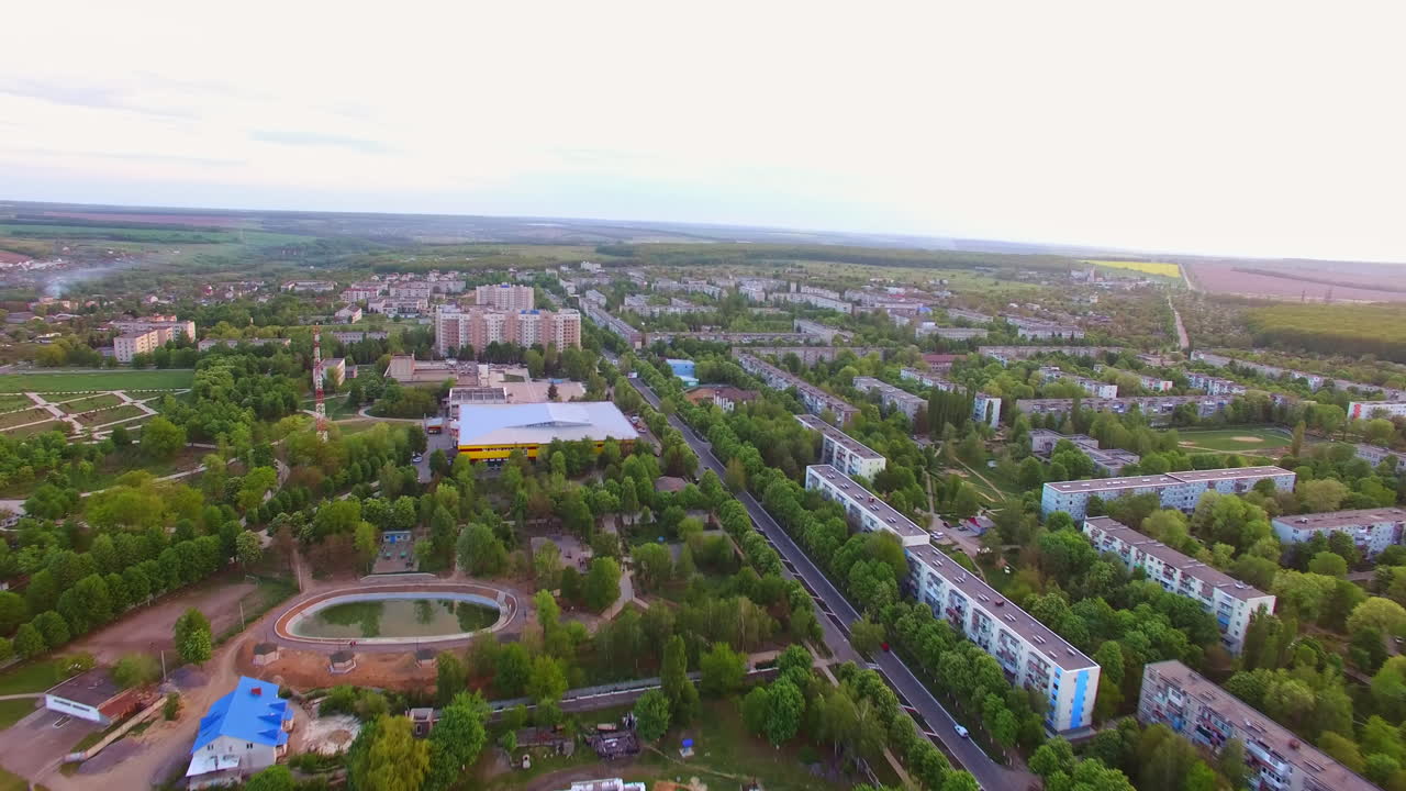 Flyover the city with beautiful green residential quarters. City park with artificial pond, stadium and lots of greenery. Top view.