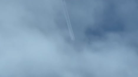 contrail of a huge military 4-engine jet flying very high shot from another airplane bellow. wake veiled by some clouds. 4k 60fps.