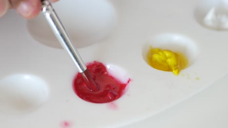 mixing red and yellow paints on a palette