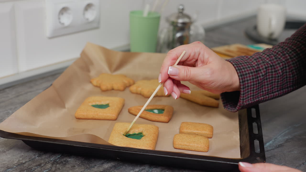 캐터러는 초록색 액체를 조심스럽게 쿠키 모양으로 조정하기 위해 지이를 사용하며 정확한 장식을 보장합니다. 다채로운 구슬을 가진 항아리를 포함한 다른 베이킹 장비가 쿠키 주변에 보입니다.