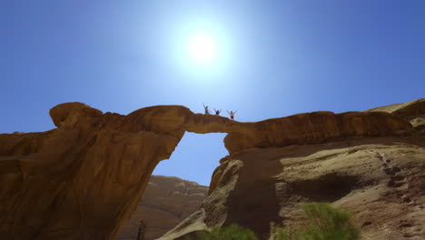 personas de pie en un arco de roca natural en el desierto