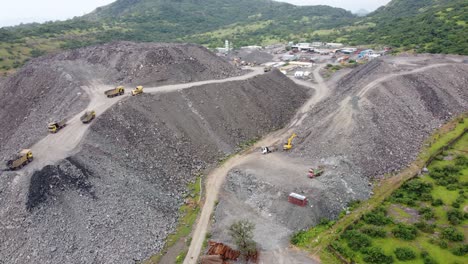 aerial view of a mountain of debris or a rubble heap with dumper trucks unloading more rock debris from a tunnelling project in a hilly region impacting the local ecology and terrain