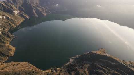 landscape at quilotoa, volcanic crater lake in ecuador, aerial drone above water calming scenic view along morning sun rays