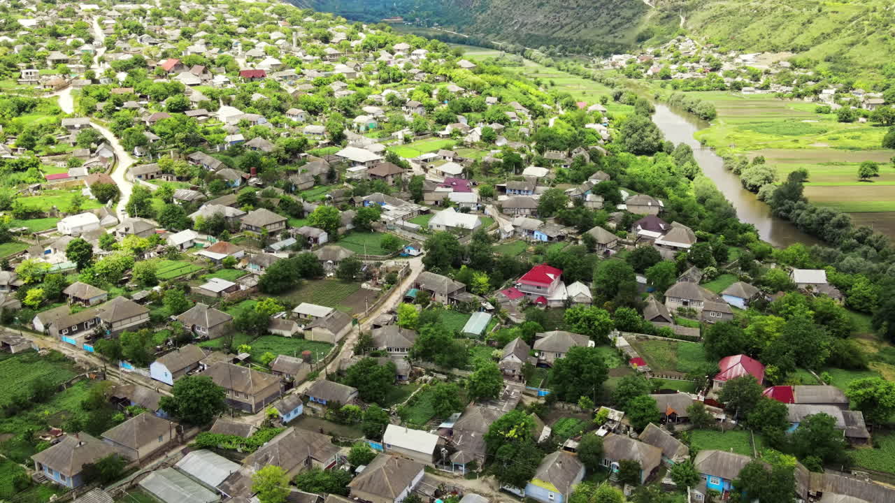 Aerial drone view of village in a valley in Moldova, multiple buildings, greenery, hills