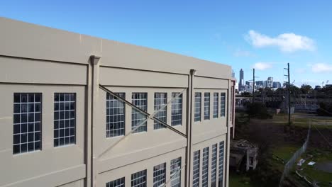 Schwenk-über-Eine-Stillgelegte-Lagerhalle-Und-Ein-Kraftwerk-In-East-Perth,-Um-Den-Blick-Auf-Die-Skyline-Von-Perth-Freizugeben