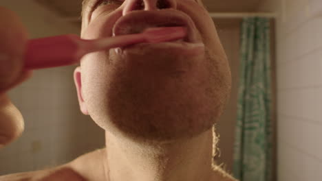 a man brushes his teeth to camera in a bathroom