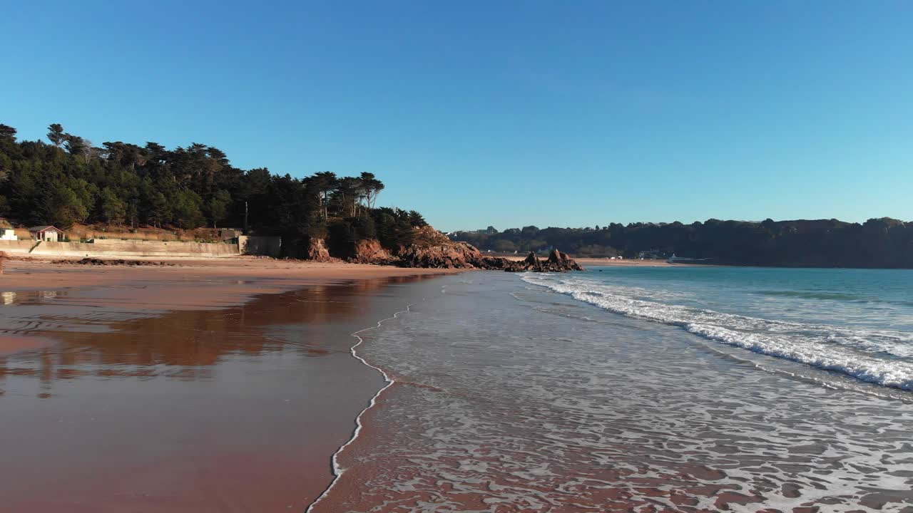 Imagem aérea de ondas quebrando em uma praia de areia, avançando.