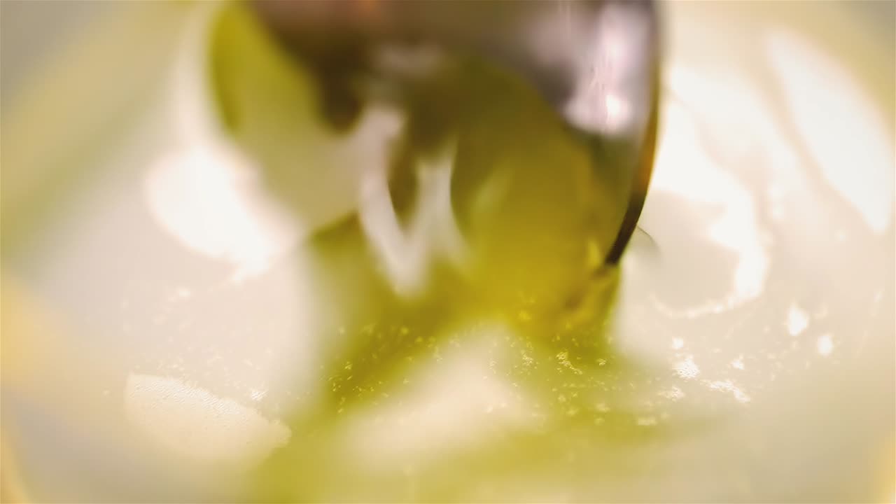 Spoon shadow reflection meets metal as yellow liquid is stirred creating mesmerizing liquified pattern