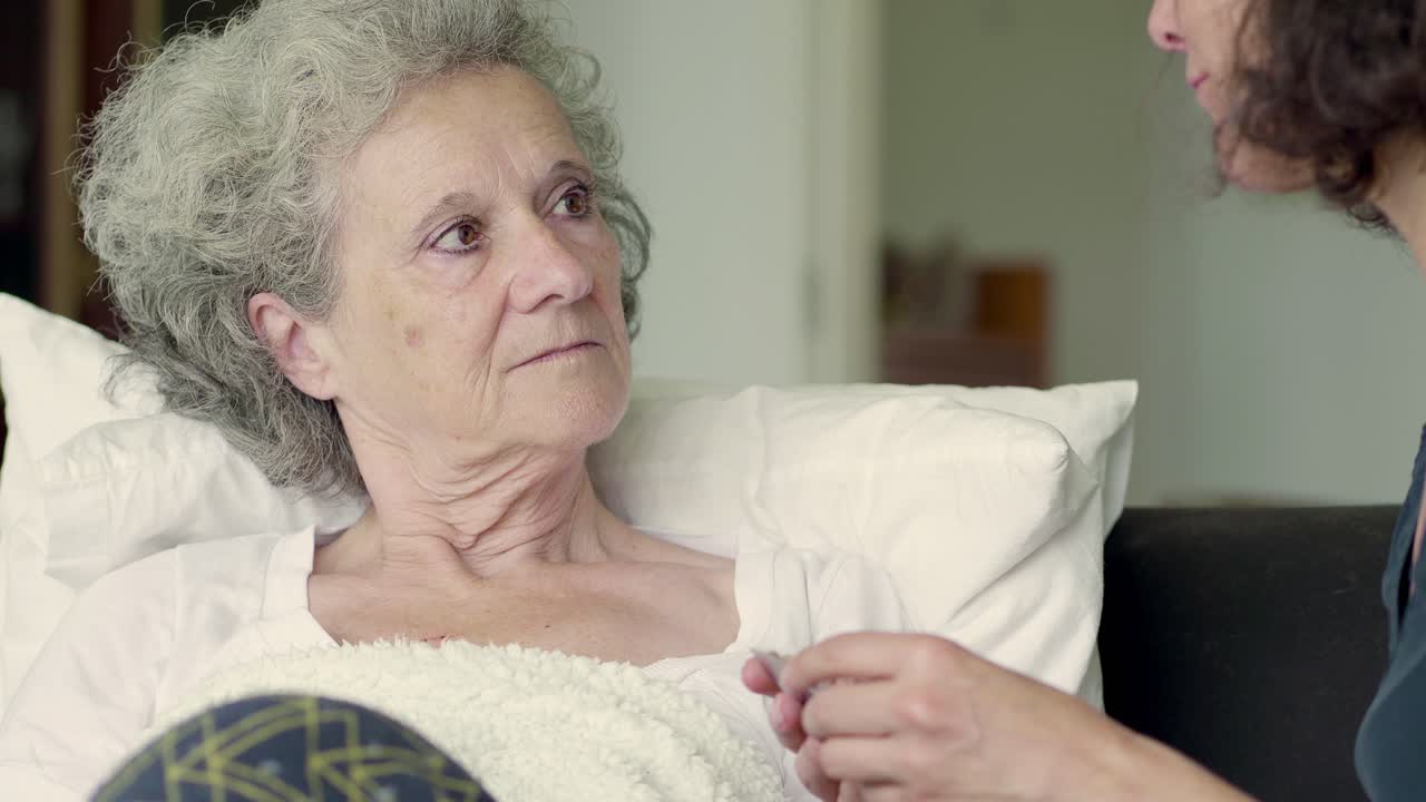 딸이 침대에 누워 있는 회색 머리 어머니에게 알약을 주는 것