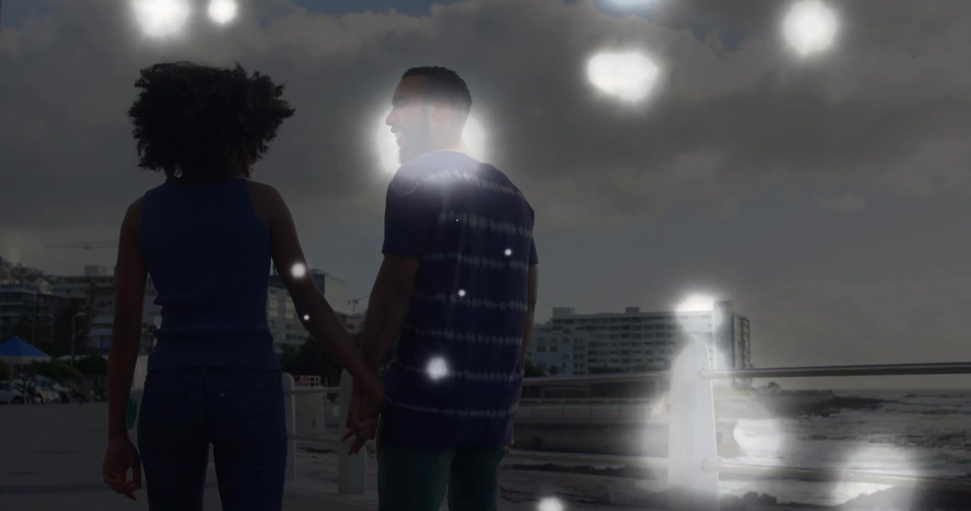 Video verticale: Coppia in jeans e maglietta a righe che cammina tenendosi per mano vicino a una ringhiera, luci fluttuanti