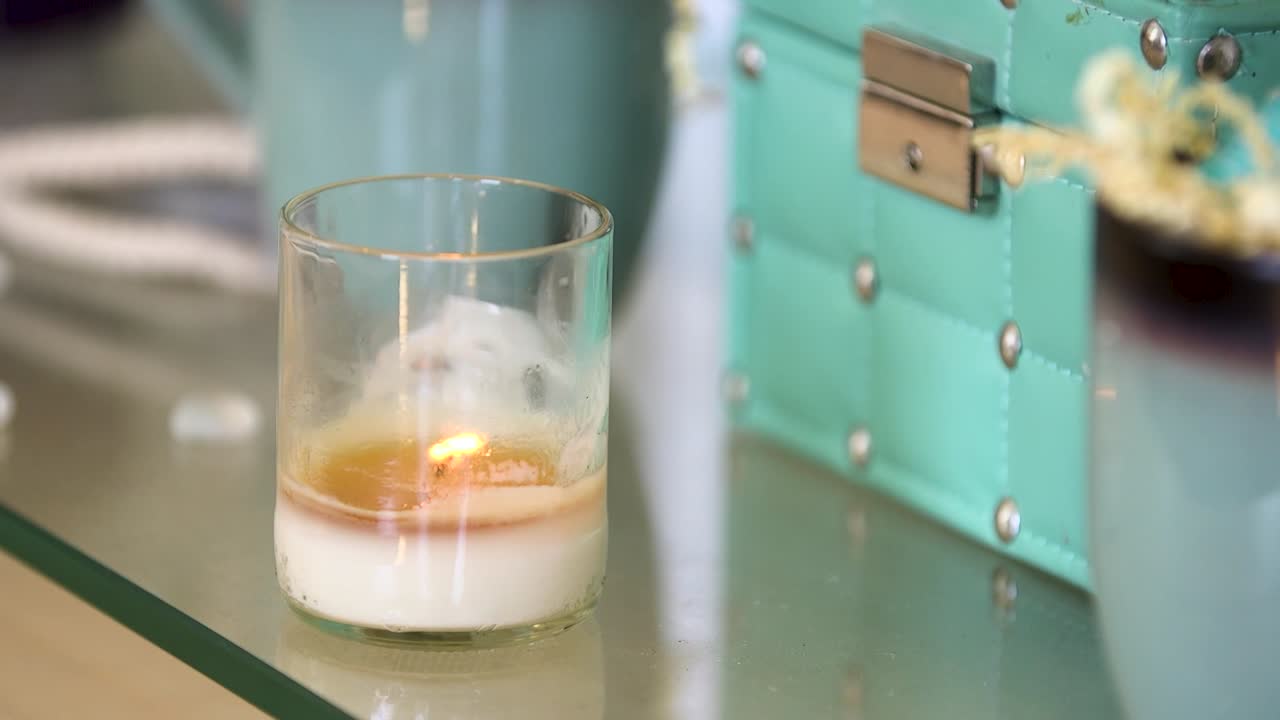 Een brandende witte kaars in een helder glas.