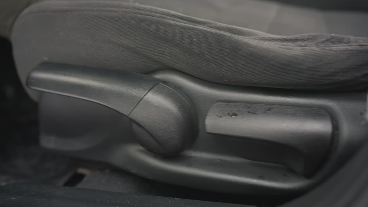 close up car seat adjustment lever and knob with small water droplets visible on surface showing seat position being changed and height being raised during winter inside vehicle interior